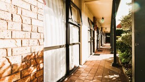 A corridor with brick walls, large windows with white curtains, and a tiled floor. - Tudor Court Motor Lodge (Auckland)