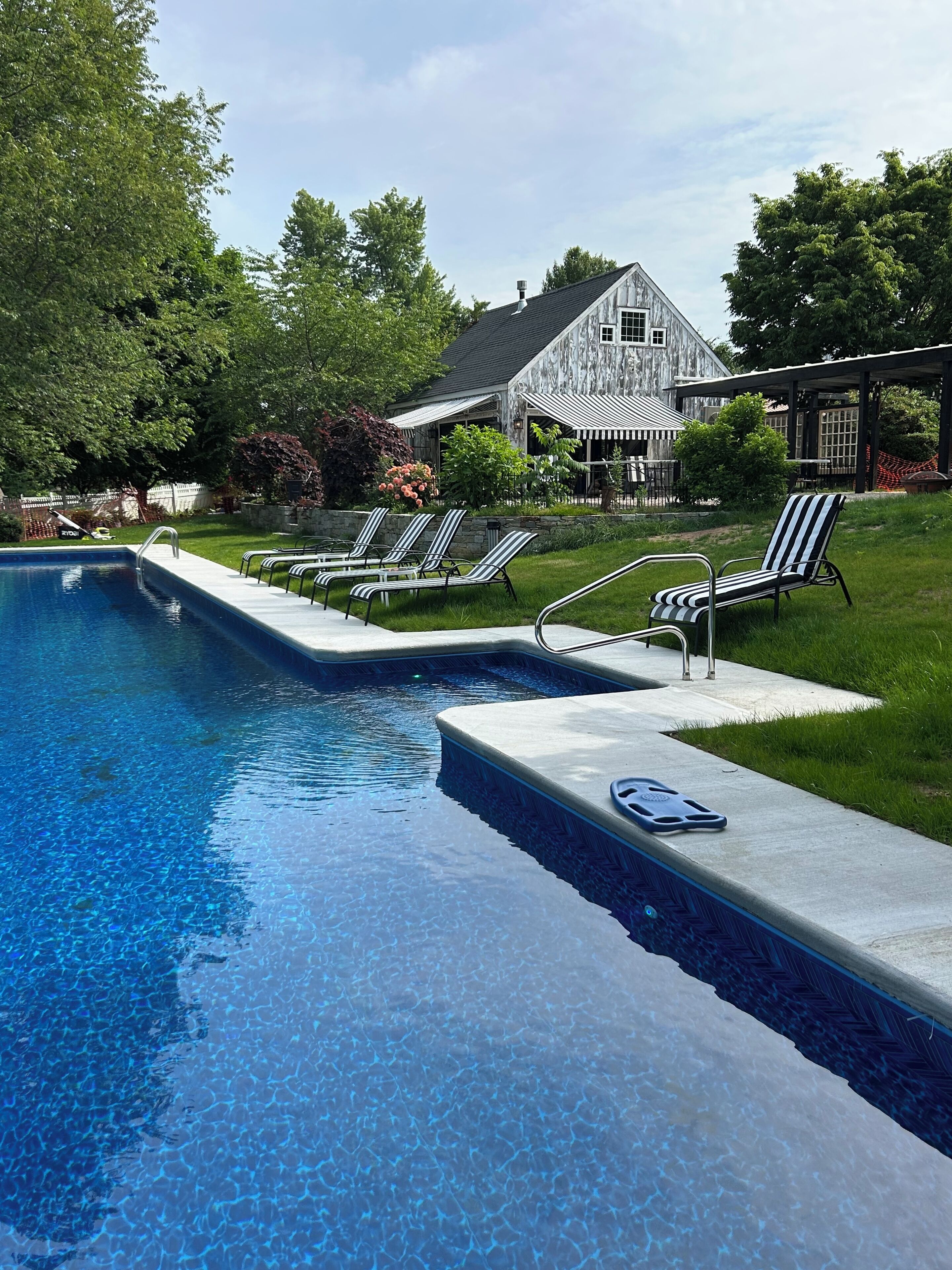 A swimming pool with lounge chairs, a stone wall, and a house in the background.