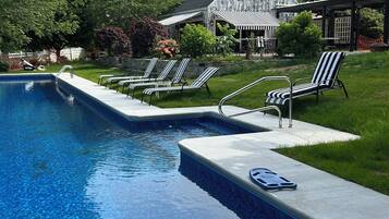 A swimming pool with lounge chairs, a stone wall, and a house in the background.