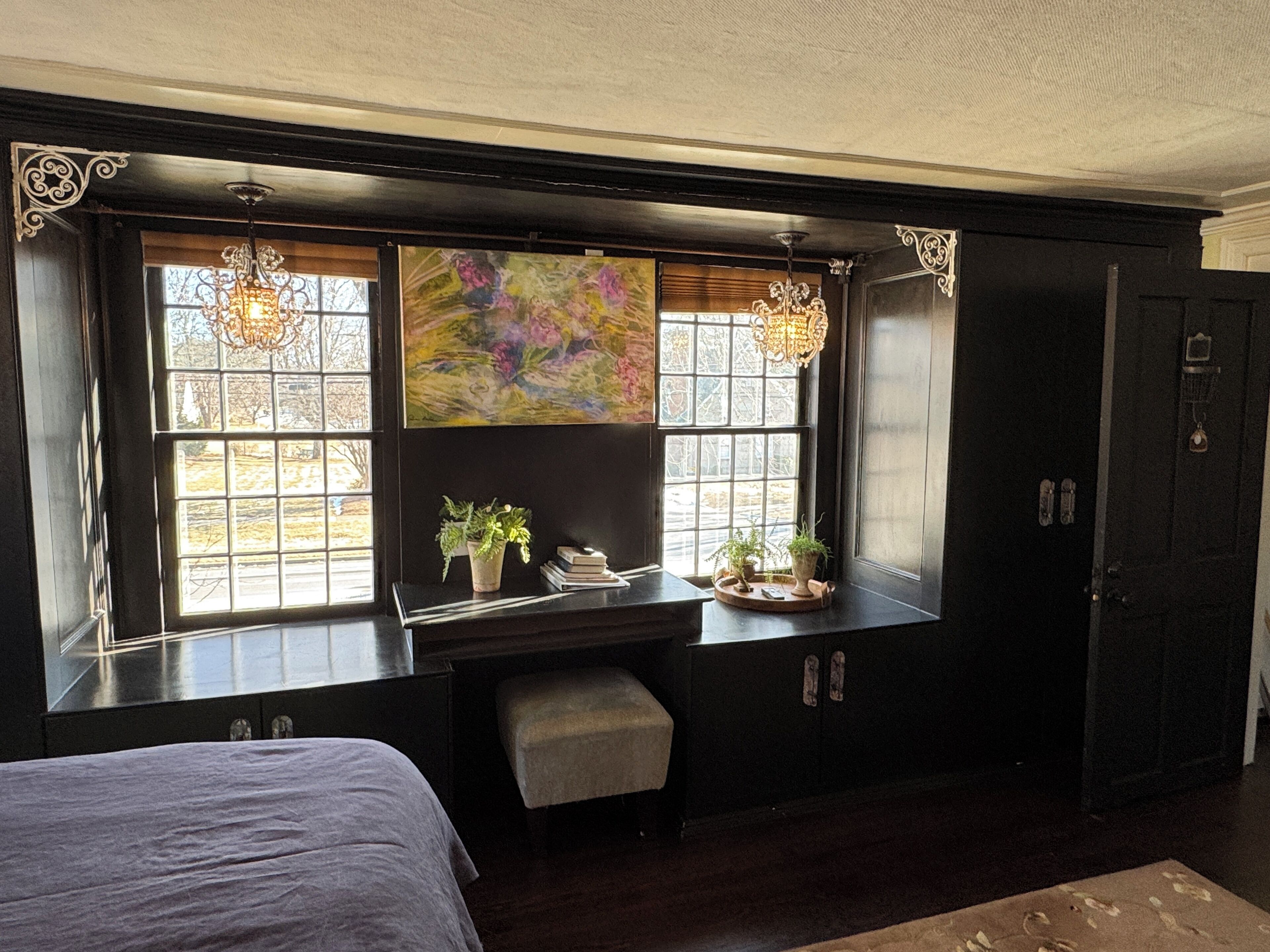 A room with a large window, a desk, two potted plants, a bench, and a wardrobe.
