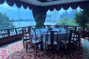 A dining area with a round table and chairs, large windows with a city view, and a patterned carpet. - Guangzhou Jiangyue Hotel (Guangzhou)