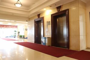 Um hall de hotel com carpete vermelho, dois elevadores e um lustre no teto.