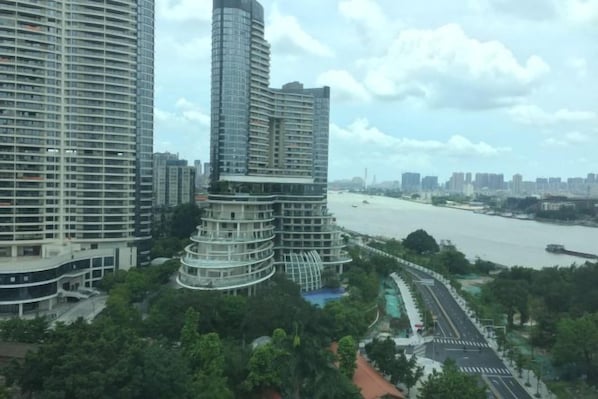 A high-rise building with a curved design, surrounded by greenery and a river.