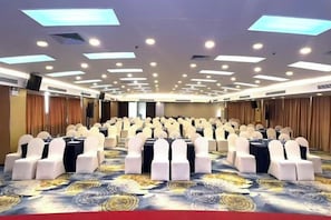 Un salón de conferencias con filas de mesas y sillas, equipado con luces en el techo y piso alfombrado.
