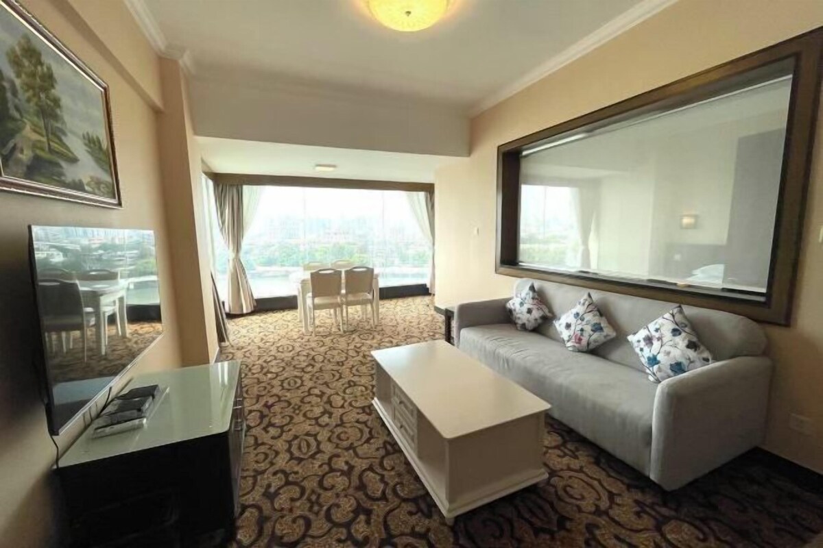 Sala de estar com sofá, mesa de centro e televisão. Tem uma varanda com vista para a cidade.