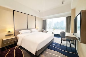 Et moderne hotelværelse med en stor seng, et skrivebord, en stol og udsigt over bybilledet gennem vinduet.