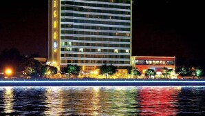 Et hotel med flere etager, oplyst skiltning, udsigt til vandet og et spejlbillede i vandet.
