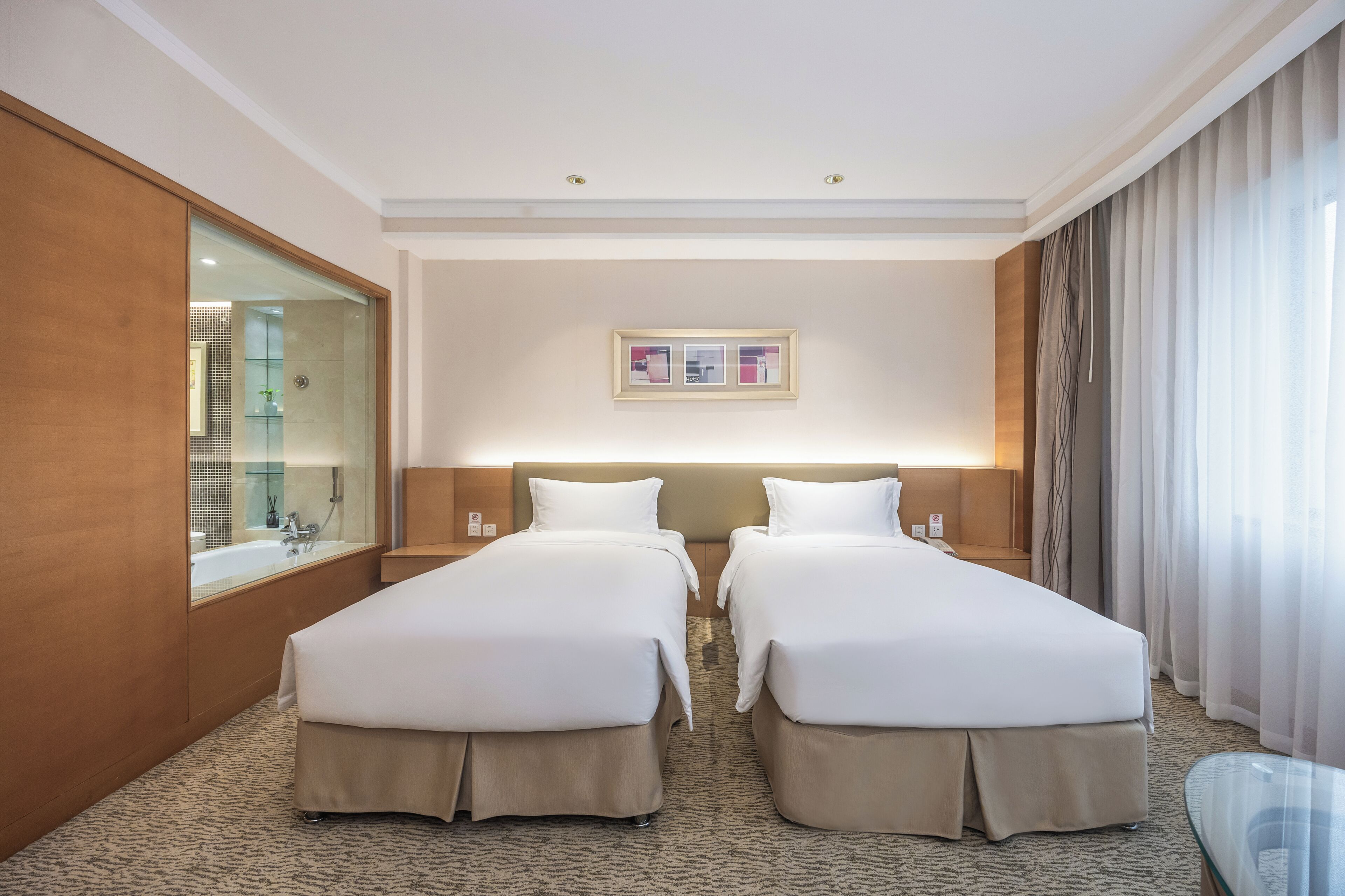 A hotel room with two beds, a large mirror, a framed picture on the wall, and a glass table.