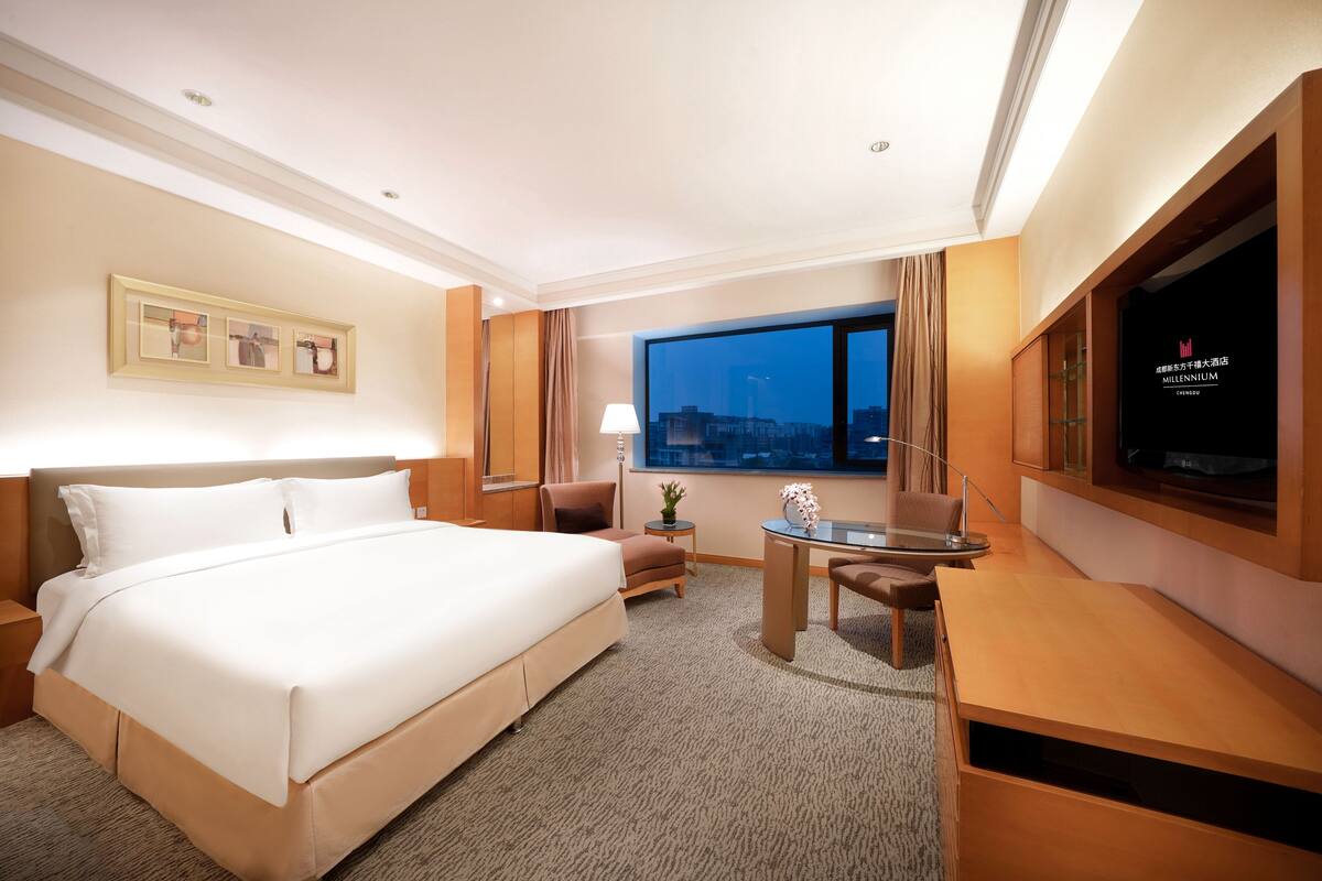 Habitación de hotel con una cama grande, un escritorio, una silla, un televisor y una ventana con vistas a la ciudad.