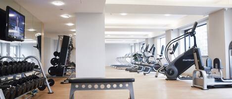 A gym with exercise equipment, a television, and a bench.