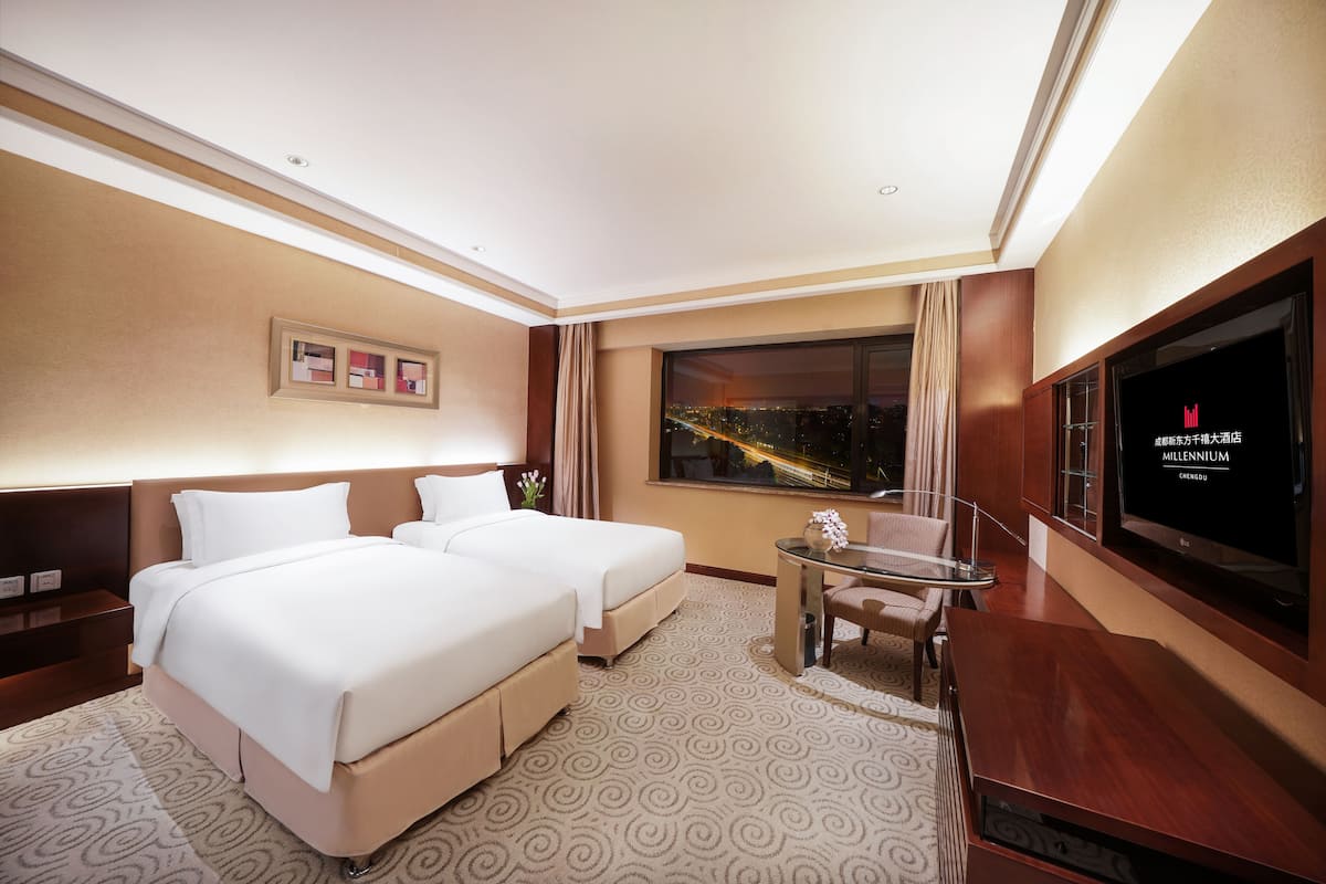 Habitación de hotel con dos camas, un escritorio, un televisor y una ventana con vista a la ciudad.