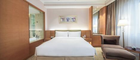 A hotel room with a large bed, a chair, a desk, a mirror, and a picture on the wall.