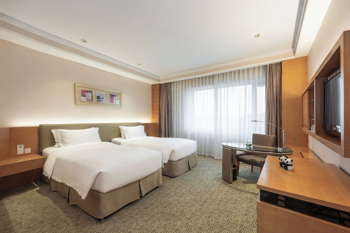 Habitación de hotel con dos camas, un escritorio, una silla, un televisor y una ventana con cortinas.