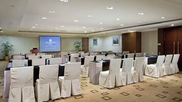 Un salón de conferencias con filas de sillas, un atril y una pantalla de proyecciones al frente.
