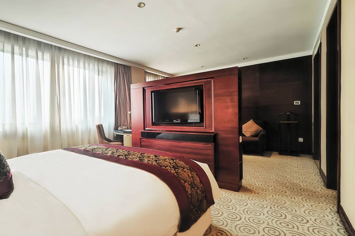 Habitación de hotel con una cama grande, televisión, escritorio y un baño visible a través de una puerta abierta.