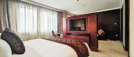 A hotel room with a large bed, a television, a desk, and a bathroom visible through an open door.