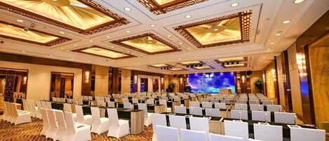 A conference room with rows of white chairs, a stage with a large screen, and a patterned carpet.