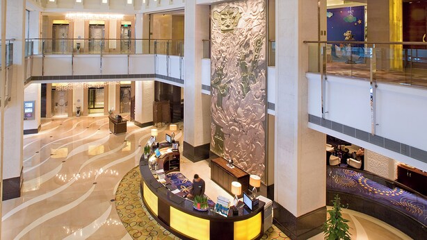 Un vestíbulo amplio con un mostrador de recepción central, varios pisos y una pared decorativa.