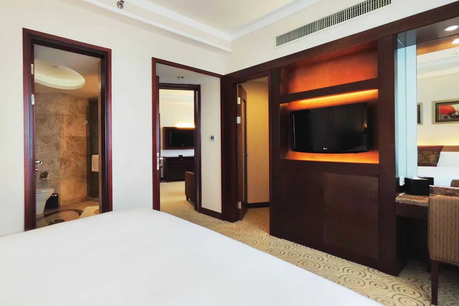 A hotel room with a large bed, a television mounted on a wooden panel, and a bathroom visible through an open door.
