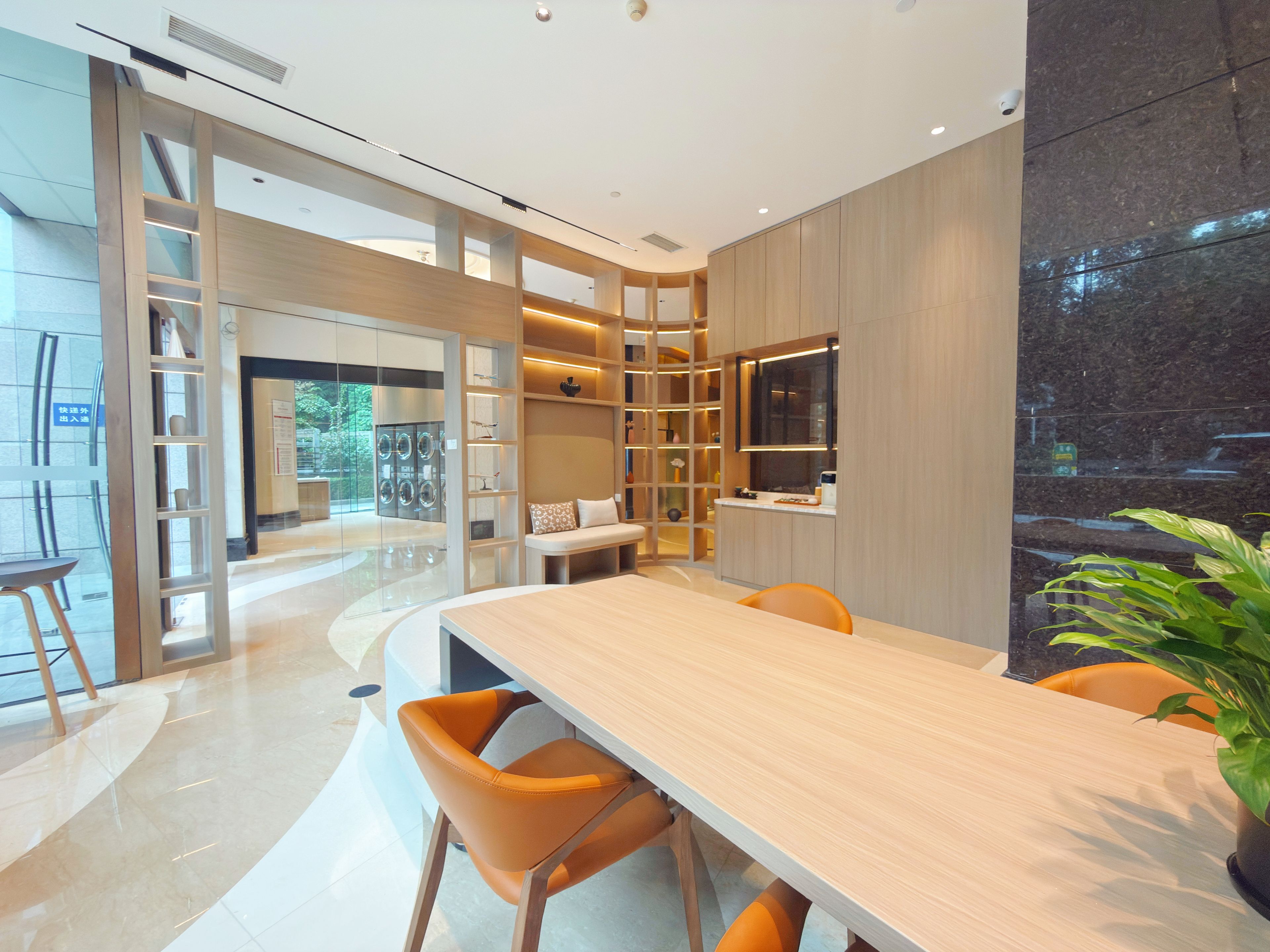 A modern interior with a long dining table, orange chairs, and a potted plant.