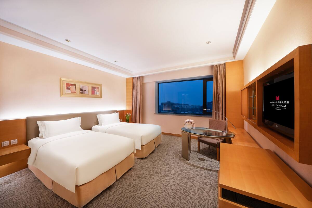 Habitación de hotel con dos camas, televisión, escritorio y ventana con vista a la ciudad.