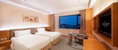 A hotel room with two beds, a TV, a desk, and a window with a city view.