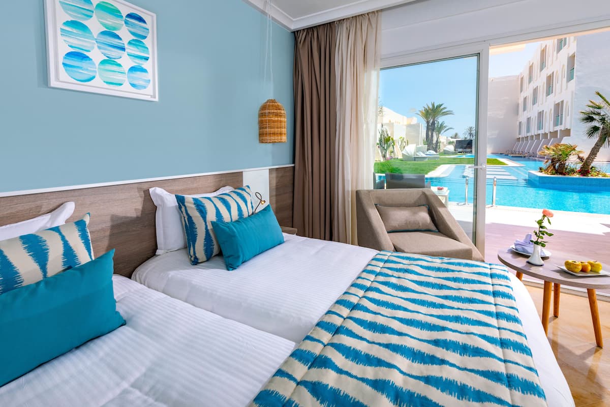 A hotel room with two beds, a view of a swimming pool, and a balcony with a table and fruit.