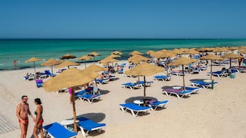 Een privéstrand, wit zand, ligstoelen aan het strand, parasols