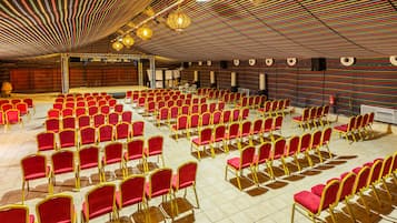 A large hall with rows of red chairs and a stage.