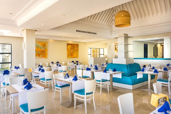 Un comedor moderno con mesas y sillas blancas, un sofá azul y obras de arte en las paredes.