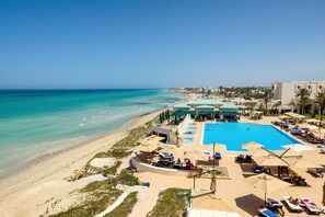 Un resort con una amplia piscina, zonas de descanso frente a la playa y vistas al océano.