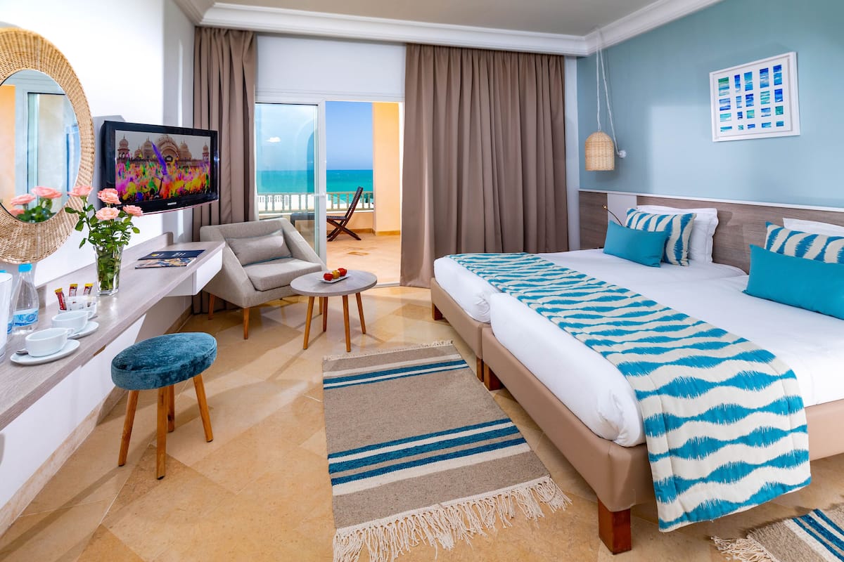 A hotel room with a bed, a desk, a chair, a TV, and a view of the ocean.