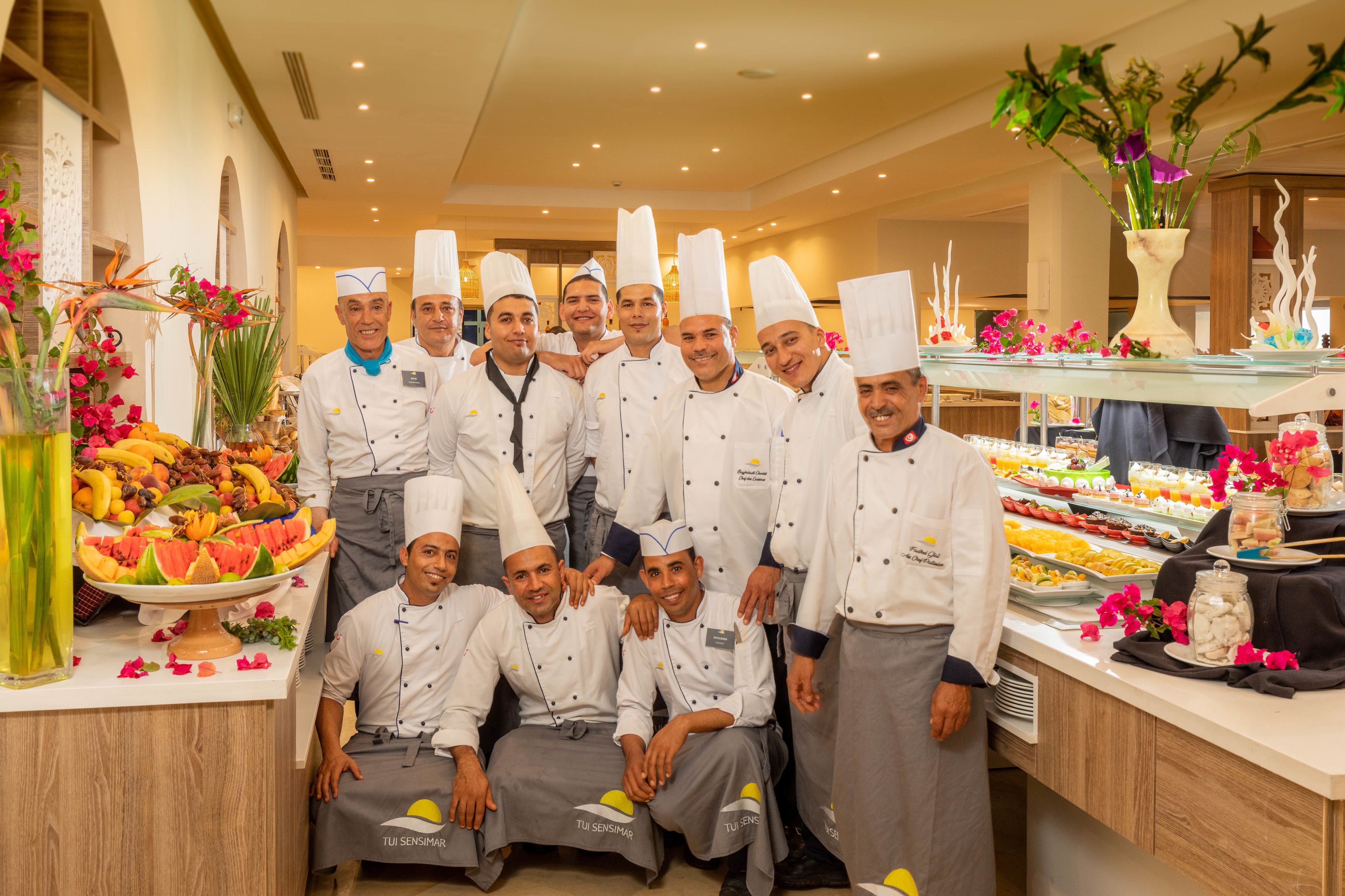 Un grupo de chefs en una cocina profesional, con diversas exhibiciones de alimentos y decoración floral.