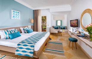 A hotel room with a bed, a sofa, a TV, a mirror, and a small table with a kettle and cups.