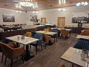 A restaurant with tables and chairs, a counter with a display case, and a chandelier.