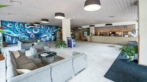 A spacious lobby with a large seating area, a reception desk, and a vibrant mural on the wall. - Hotel Cascade (Most)