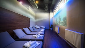 A spa room with multiple massage tables, a wall-mounted aquarium, and a radiator. - Hotel Cascade (Most)