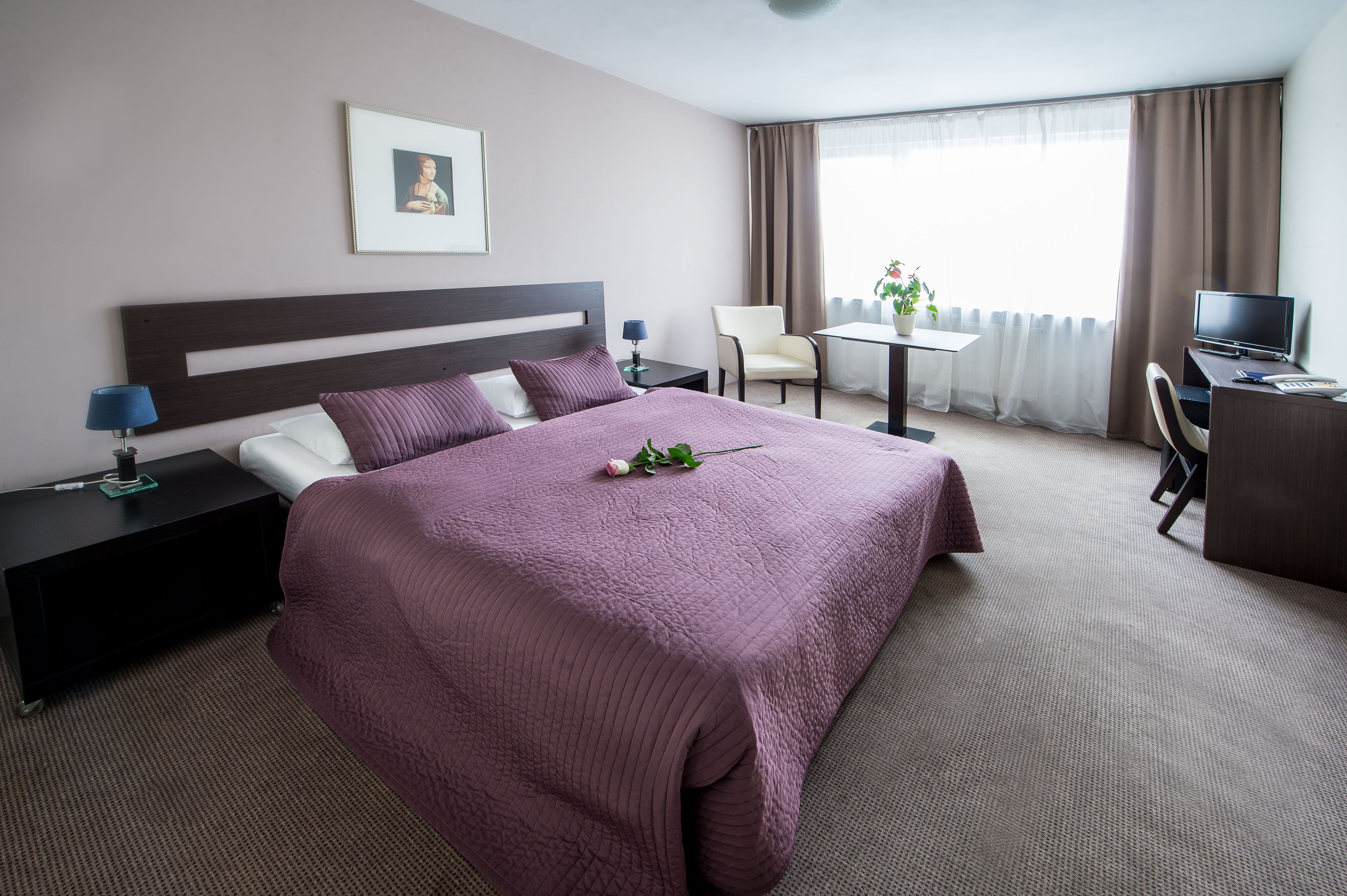 A hotel room with a large bed, a desk with a computer, a chair, and a TV.