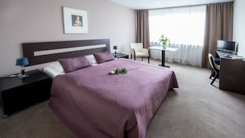 A hotel room with a large bed, a desk with a computer, a chair, and a TV.