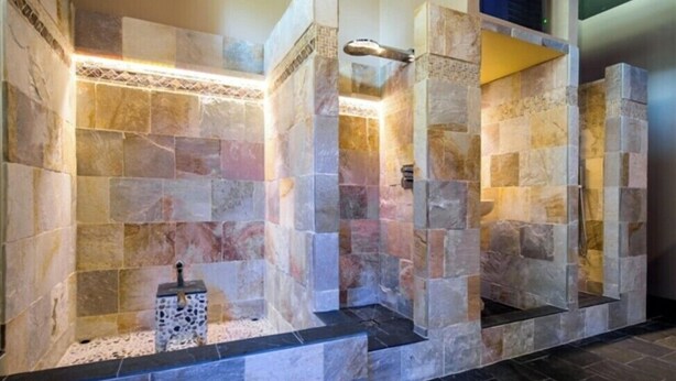 A stone-walled bathroom with a built-in shower and a small decorative item on the floor. - Hotel Cascade (Most)