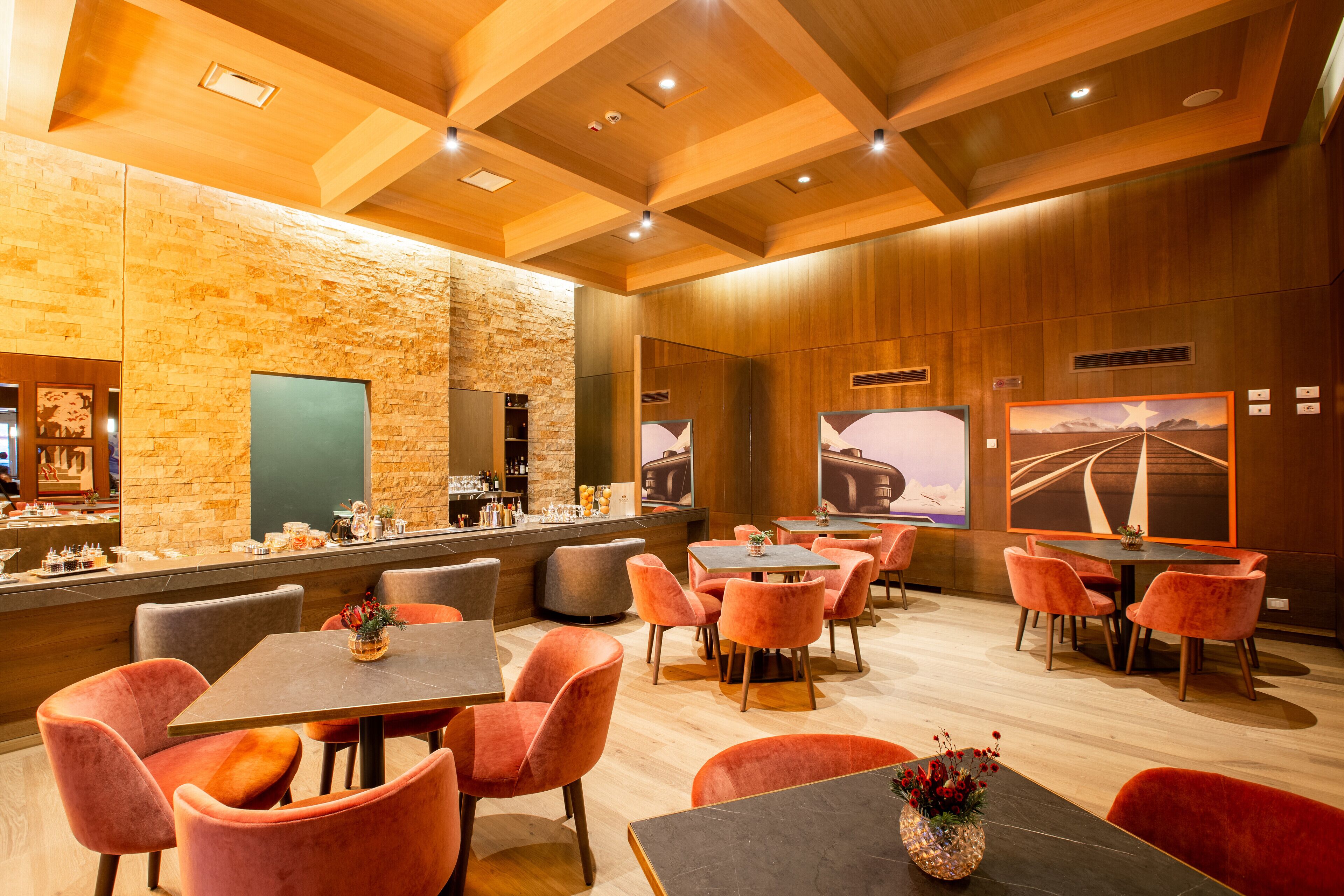 A modern restaurant with wooden ceilings, stone walls, and orange chairs. Tables are arranged for dining.