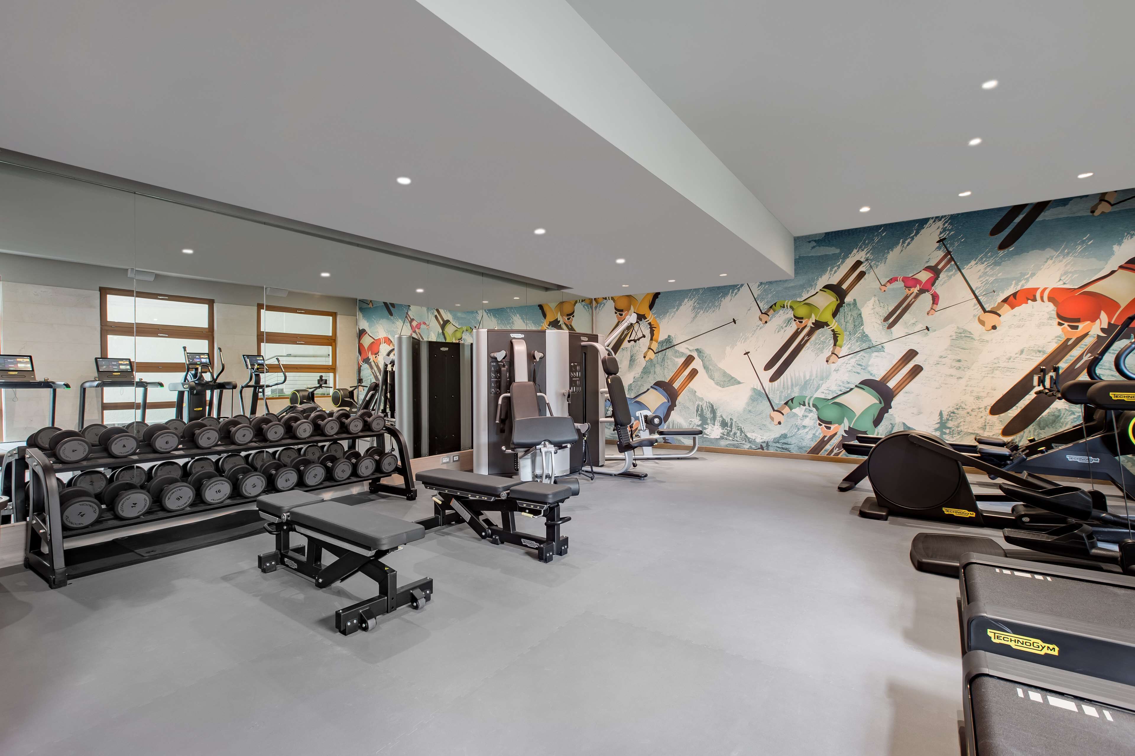 A gym with various exercise equipment, including dumbbells, benches, and cardio machines.