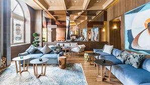 En modern hotellobby med en blå soffa, runda bord och en stor, abstrakt målning.