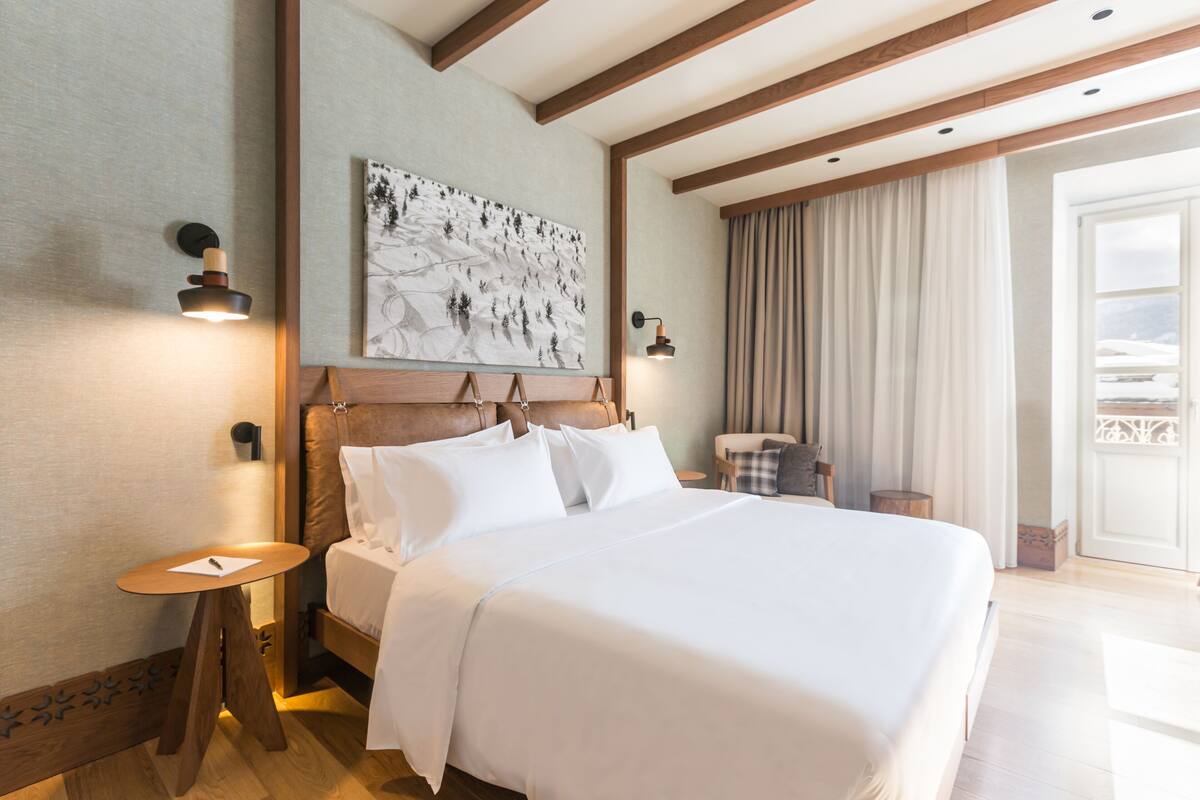 Camera d'albergo con un letto grande, una testiera in legno, due comodini, un'opera d'arte appesa al muro e vista sull'esterno attraverso una finestra.
