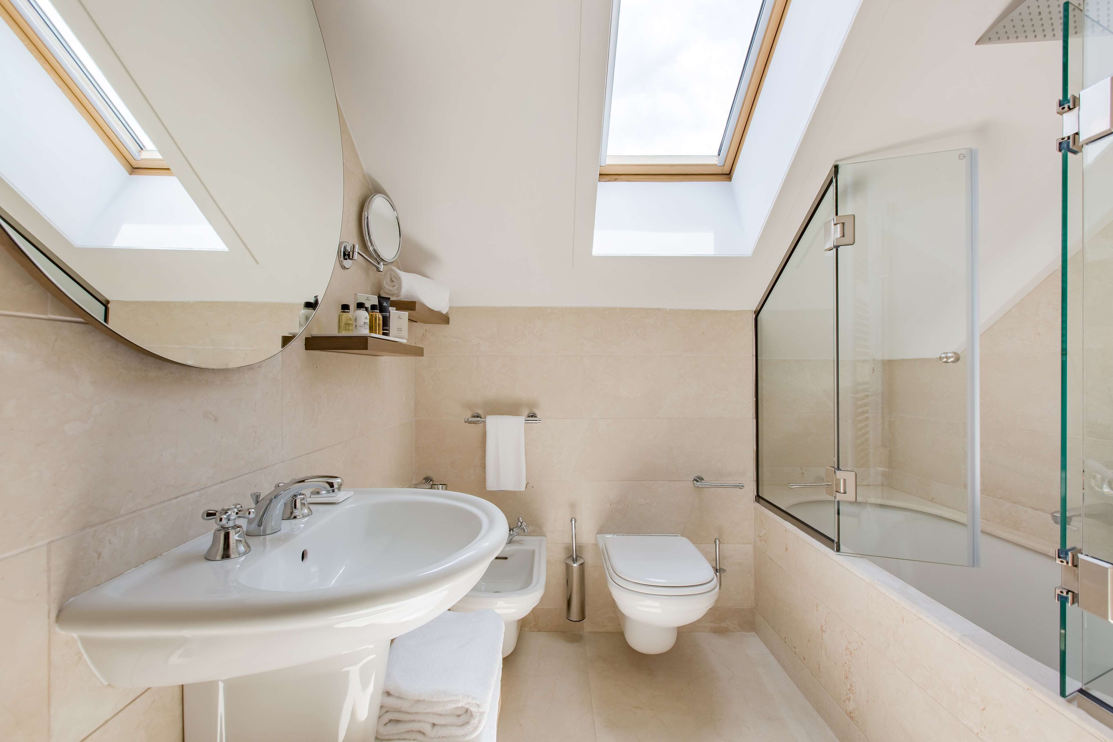 A modern bathroom with skylights, a large sink, a bidet, and a glass-enclosed shower.