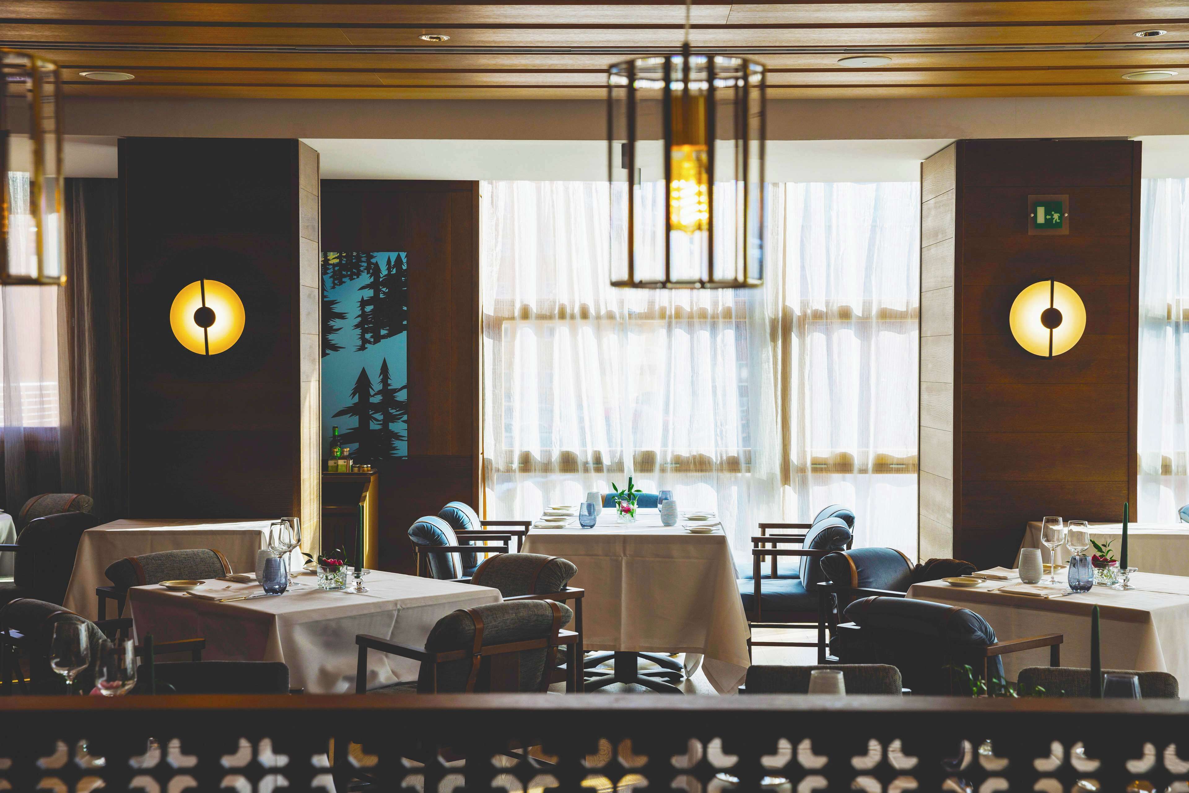 Un restaurante con varias mesas, cada una con mantel, sillas y cubertería.