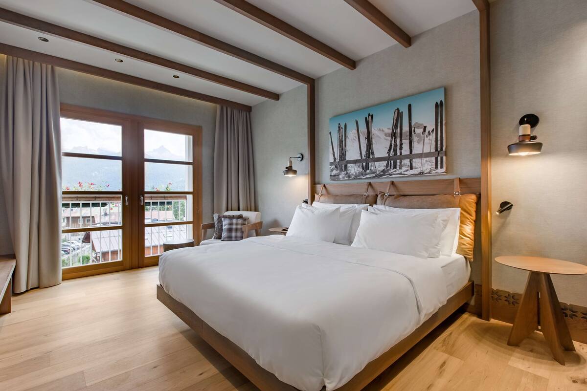 Un'ampia camera da letto con un letto grande, vista attraverso le porte scorrevoli, un quadro con sci appeso al muro e un piccolo tavolino rotondo.