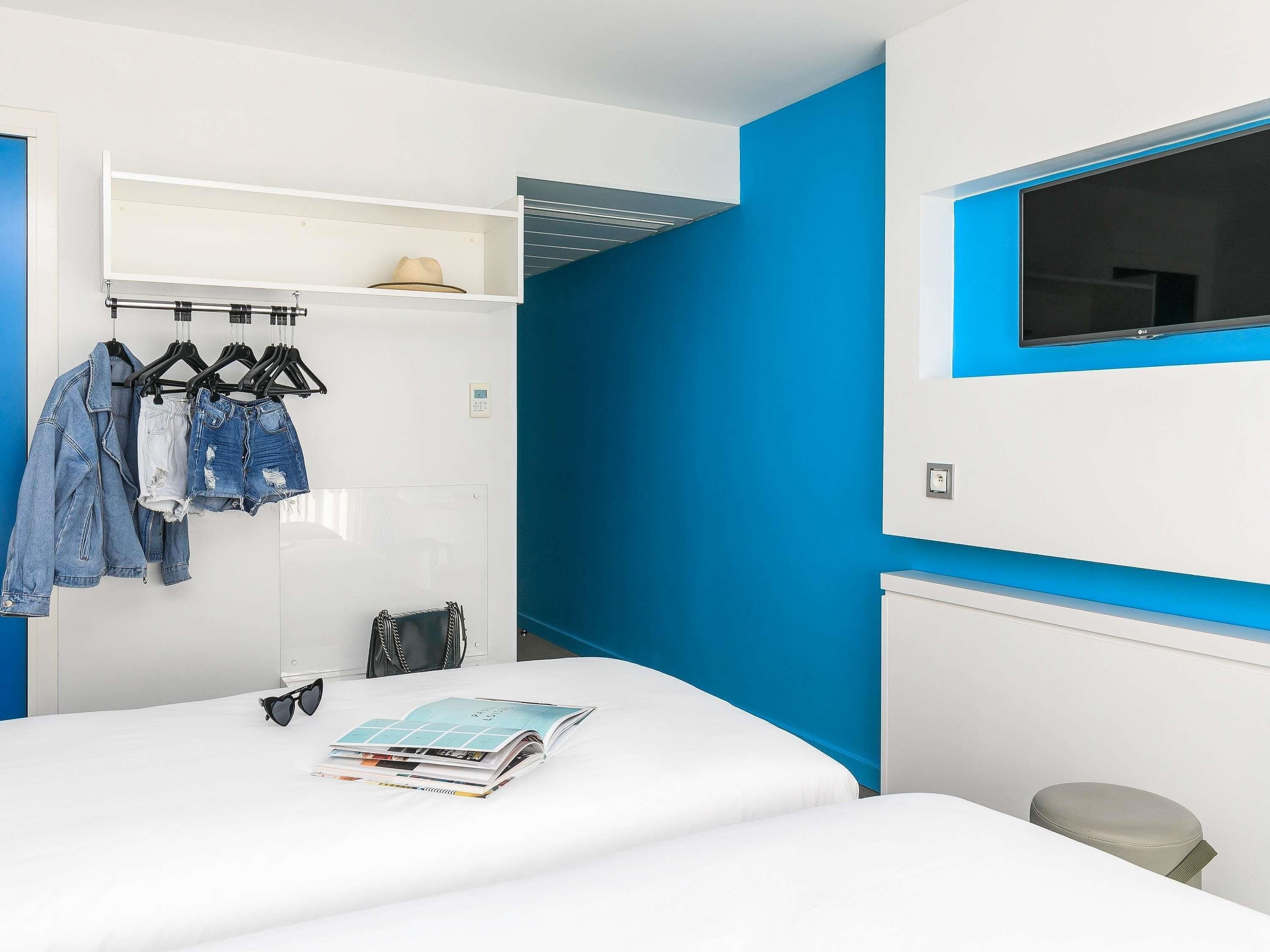 A bedroom with a bed, a wardrobe, a hanging shoe rack, a TV, and a window.