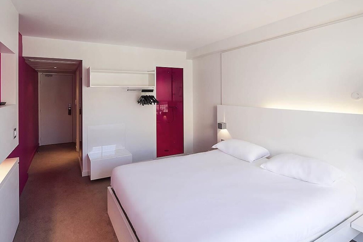 Ein Hotelzimmer mit einem großen Bett, einem Nachttisch, einem Kleiderschrank und einem Badezimmer mit Dusche.