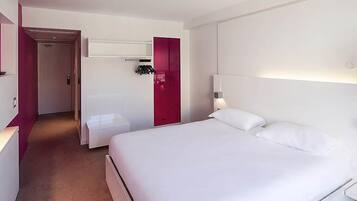 A hotel room with a large bed, a bedside table, a wardrobe, and a bathroom with a shower.